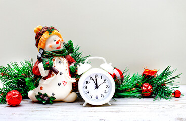 On a light gray background, a beautiful snowman, a white alarm clock and fir branches with New Year's balls and gifts. Christmas concept. Copy space.