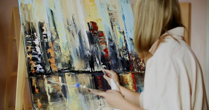 Woman painting fine art abstract landscape with palette knife oil paints on canvas in creative studio. Female painter drawing with oil paints on canvas in art workshope