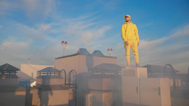 Dancing man in yellow bright outfit breakdancing on rooftop. Hiphop bboy dancer performing stunts enjoying dance on sunny day morning.