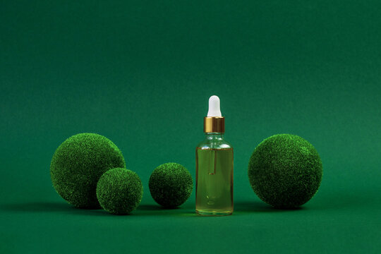 Creative green background. A glass jar with cosmetic oil and a pipette. Protector skin Treatment facial essence oil, Vitamin C. Beauty and spa Concept. Concept scene stage for promotion, presentation
