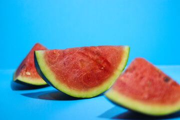 Fototapeta na wymiar Close-up view of fresh ripe watermelon slices on blue background. Tropical fruits, healthy eating, and summer background concept.