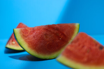 Close-up view of fresh ripe watermelon slices on blue background with highlight and shadow contrast in the morning. Tropical fruits, healthy eating, and summer background concept.