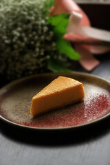 Fruit or vegetable orange cheesecake in a clay plate against the backdrop of a bouquet of flowers.
