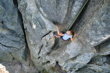 Determined boy climber clambering up steep wall of rocky mountain. Child overcoming difficult route. Engaging in extreme sports and rock climbing hobby concept.