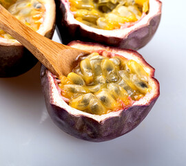Three halved passion fruits on white background, wooden spoon filled with pulp inside one half,...