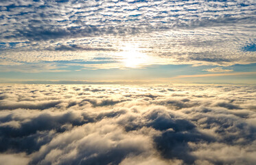 Fototapeta na wymiar Aerial view of vibrant yellow sunrise over white dense clouds with blue sky overhead.
