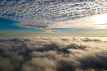 Aerial view of bright yellow sunset over white dense clouds with blue sky overhead.