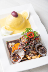 Black peel eviction, accompanied by huancaína potatoes, on a white plate.
