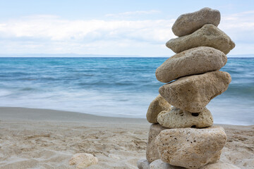 Fototapeta na wymiar Zen stones stack balanced on beach with sea and clear blue sky in background