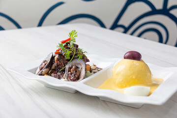 Black peel eviction, accompanied by huancaína potatoes, on a white plate.
