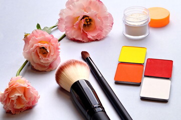 Obraz na płótnie Canvas face powder, eyeshadow and brushes lie on the table surrounded by amazingly beautiful flowers