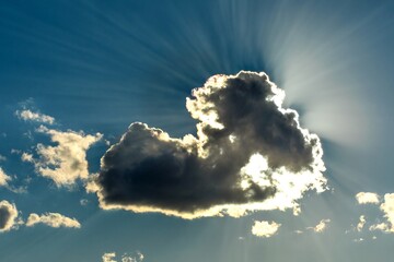 Sun is shining from behind clouds. Blue sky with clouds and sunbeams. Sun hidden behind a cloud.