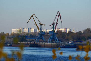 Obraz premium River port. Construction site on the river bank. A harbor crane loads sand onto a barge.