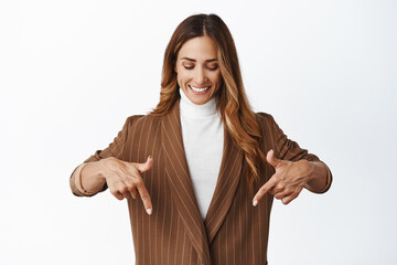 Smiling successful businesswoman pointing and looking down with pleased face, choosing, showing something below, white background