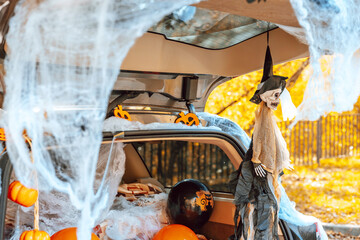 cute trunk of car decorated for Halloween with cobwebs, orange balloons, pumpkins and sweets, the...