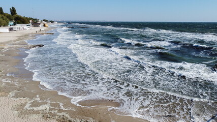 Aerial drone view flight over sea waves that roll onto sandy shore.