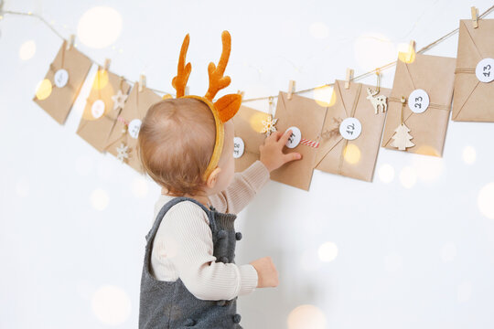A baby dressed up party clothes and a hand-made advent calendar. Preparation to Christmas. Craft envelopes with numbers arranged on wall.