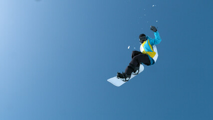 Fototapeta na wymiar BOTTOM UP: Male snowboarder does a spectacular grab trick high in the air.