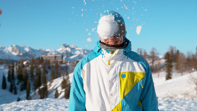 CLOSE UP: Stoked male snowboarder gets hit in the head by a large wet snowball.