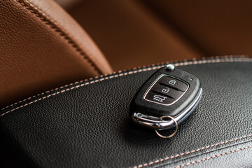 Modern wireless car key on darl leather in car interior. Remote control key in vehicle close up view..