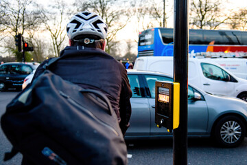 Rear view of cyclist with helmet waiting at the crossroad pedestrians street crossing with light on on the semaphore with wait illuminated text