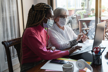 Multi generational young and senior business people with safety masks working inside modern office - Focus on old woman face