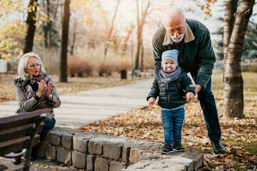 Happy senior couple walking and playing with their adorable grandson in public city park.