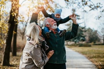 Happy good looking senior couple husband and wife walking and playing with their adorable grandson...