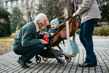 Obraz na płótnie Canvas Happy good looking senior couple husband and wife walking and playing with their adorable grandson in public city park