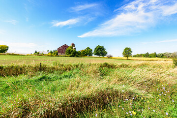 Old barn in a farm field under blue sky with white clouds in rural area in Ontario, Canada