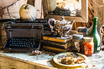 Still life, antique typewriter, old books, silver tea pot, glass jars, green bottle, herbs, seeds, pumpkin, mirror on antique white table with cracks, natural light, sun beams