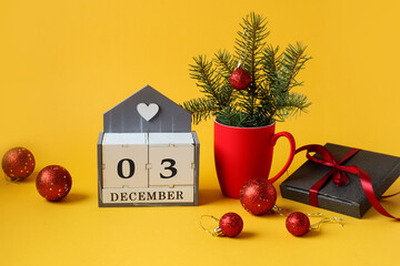 Calendar for December 3 : the name of the month in English, the numbers 0 and 3 ,a Christmas composition in a red cup, Christmas balls, a gift in a gray package, tied with a red ribbon