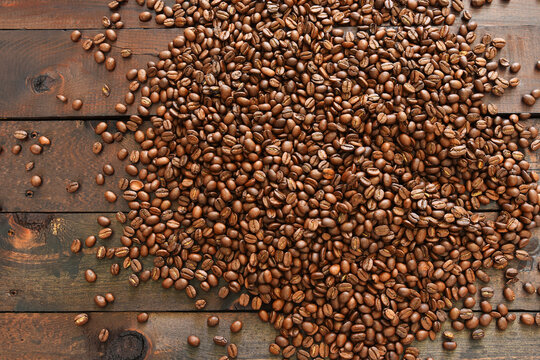 A top view image of dark roasted coffee beans spilled on a dark wooden table top.