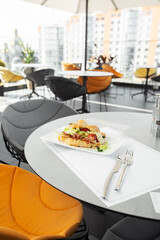 Croissant sandwich with bacon, tomatoes and lettuce salad on white plate and bright background. Continental style breakfast.
