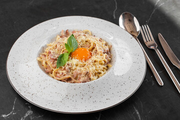 Pasta Carbonara. Spaghetti with bacon, parmesan, cream sauce and egg yolk on black marble background. Mediterranean gourmet food.