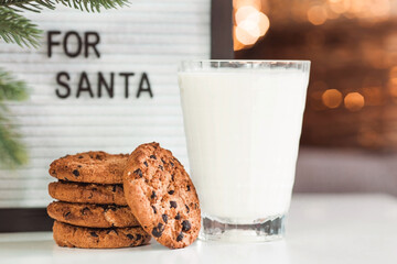 Merry Christmas 2022. Beautiful background with chocolate chip cookies and a glass of milk for Santa Claus. Celebrating the winter New Year holidays. The concept of the beginning of the year.