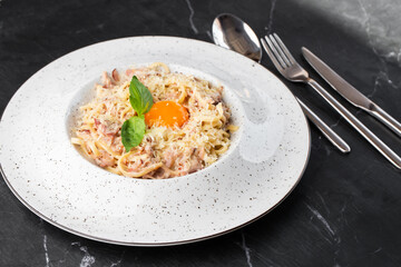 Pasta Carbonara. Spaghetti with bacon, parmesan, cream sauce and egg yolk on black marble background. Mediterranean gourmet food.