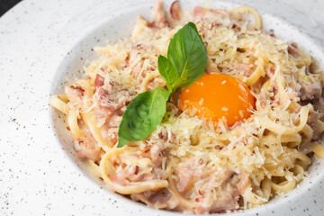 Pasta Carbonara. Spaghetti with bacon, parmesan, cream sauce and egg yolk. Macro close-up isolated on a white round plate. Mediterranean gourmet food.