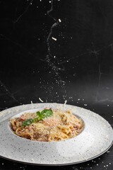 Cheese falling on pasta. Spaghetti with bacon, parmesan, cream sauce and egg yolk on black marble background. Mediterranean gourmet food.