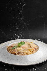 Cheese falling on pasta. Spaghetti with bacon, parmesan, cream sauce and egg yolk on black marble background. Mediterranean gourmet food.