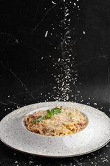Cheese falling on pasta. Spaghetti with bacon, parmesan, cream sauce and egg yolk on black marble background. Mediterranean gourmet food.