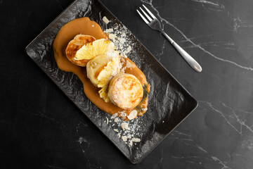 Cottage cheese pancakes, Syrniki or Cheesecakes with dried pineapple and caramel isolated on black marble background. Homemade food. Tasty breakfast. Selective focus.