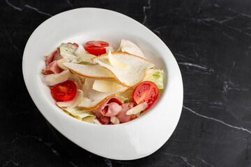Caesar Salad. Grilled bacon, tomatoes, croutons, parmesan and fresh salad in plate. On black marble background.