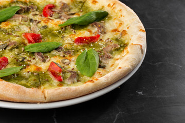 Delicious hot homemade pizza on black marble table. Pizza - Fresh homemade pizza with meat, cheese, tomato sauce, tomatoes, pumpkin seeds and basil.