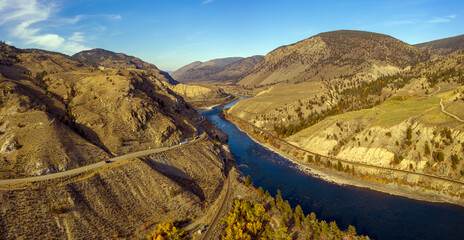 Aerial panoramic view of the Thompson river bending in its bed throughout a breathtaking mountainous landscape alongside Highway 1 in Thompson-Nicola Regional District, British Columbia, Canada