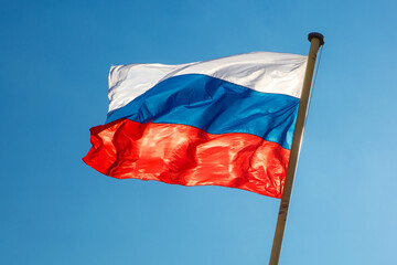 Russian flag against blue sky waving in the wind.