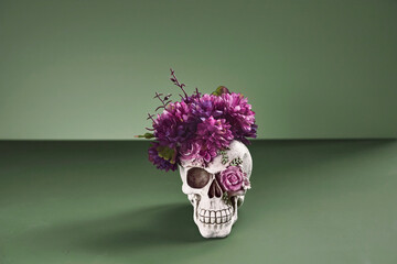 Day of The Dead skull adorned with purple flowers. On pastel dark green background with copy space - 464600650
