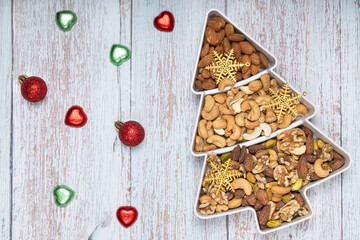 Mixed nuts and gold Christmas ornaments in a pine shape plate on light blue wooden background.