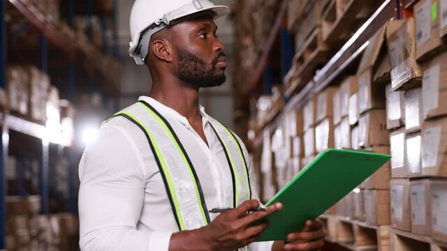 Black male staff working and checking inventory stock at large depot warehouse store or shipping distribution center, slow motion