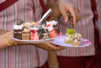 Close up of woman's hand holding plate of various mini cakes while choosing for takeout at bakery store in outdoor market